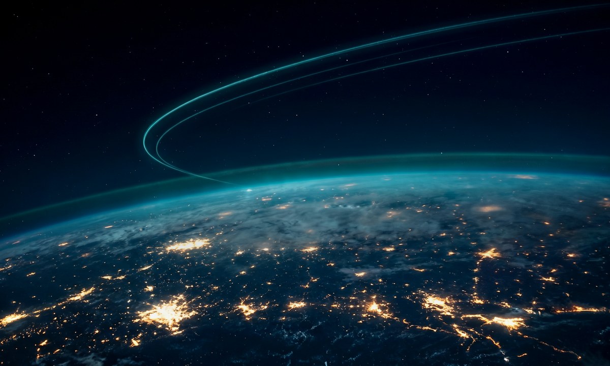 Earth from low orbit at night with city light clusters glowing across the curve and cyan satellite arcs sweeping overhead